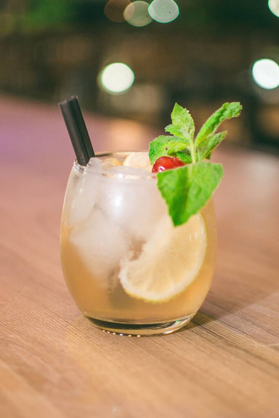 A cold beverage with ice cubs, mint leaves, a cherry and a black straw - Photo, Image