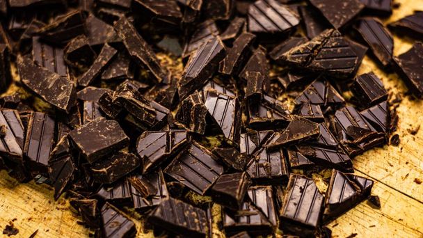 A closeup of chopped dark chocolate pieces on a wooden surface - Фото, зображення