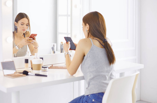 Incroyable jeune femme qui se maquille devant un miroir. Portrait de belle fille près de la table cosmétique. - Photo, image