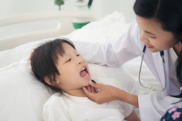 Woman doctor examining little girl mouth at hospital checking the sore throat of a young patient - 写真・画像