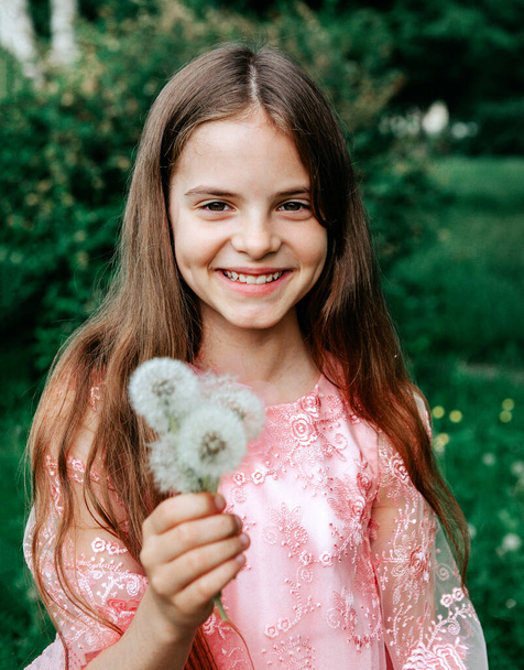 Adolescente de 10 años con el pelo largo en un vestido rosa con dientes de león sobre un fondo verde
 - Foto, imagen