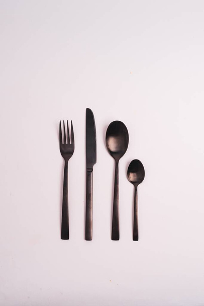 A vertical shot of two spoons, a knife, and a fork isolated on a light-colored background - Photo, image