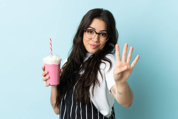 Jeune femme avec milkshake fraise isolé sur fond bleu heureux et comptant quatre avec les doigts - Photo, image