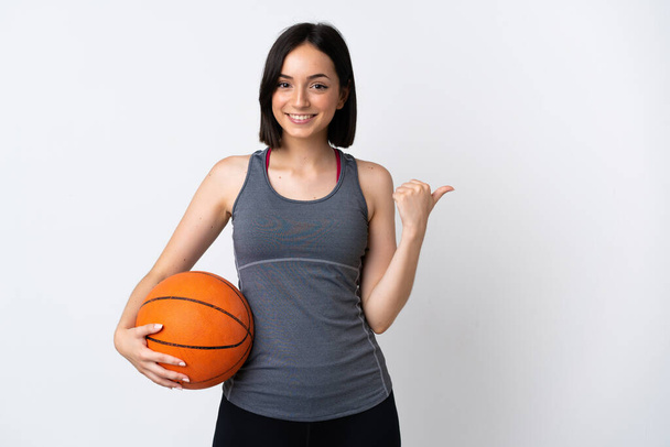 プロダクトを提示するために側面を指す白い背景に孤立したバスケットボールをプレイ若い女性 - 写真・画像