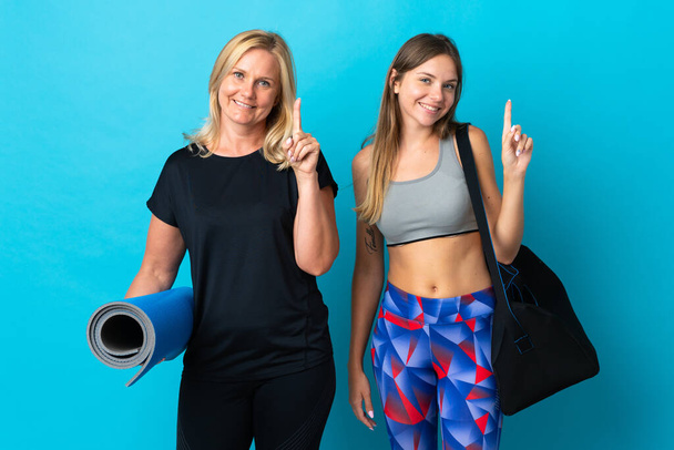 Mom and daughter doing yoga isolated on blue background showing and lifting a finger in sign of the best - Foto, imagen