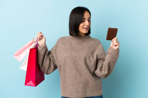 Молодая белая женщина, изолированная на синем фоне с сумками для покупок и кредиткой. - Фото, изображение