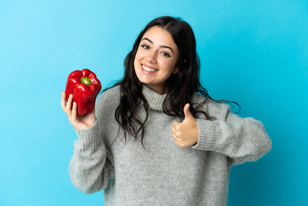 Young caucasian woman holding a pepper isolated on blue background with thumbs up because something good has happened - Fotoğraf, Görsel