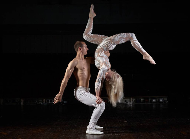 A sports couple of acrobats performs the trick. Acrobats on a dark background. - Photo, Image