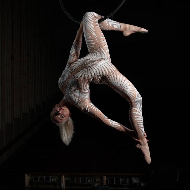 De acrobaat voert een stunt uit op de luchtring. Meisje in een pak voor optredens. - Foto, afbeelding