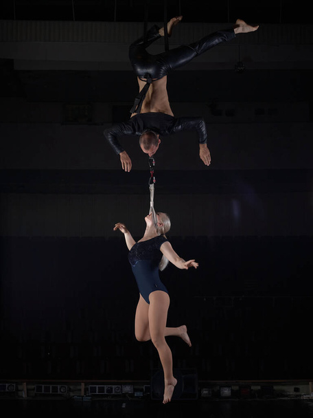 A sports acrobat couple performs a trick in the air. Acrobats on a dark background. - Photo, Image