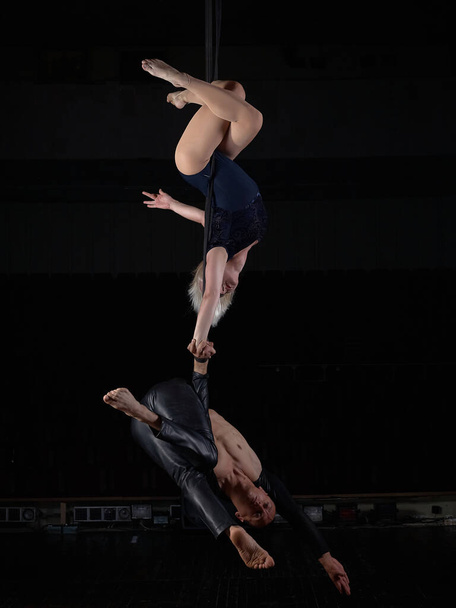 Een sportief acrobaat koppel doet een truc in de lucht. Acrobaten op een donkere achtergrond. - Foto, afbeelding