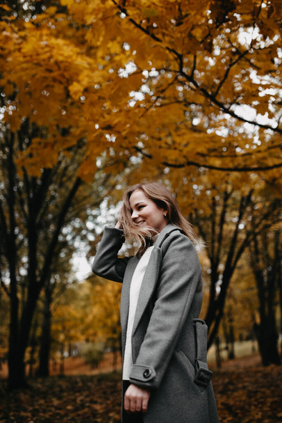 Young woman in a gray coat walking in autumn forest  - 写真・画像