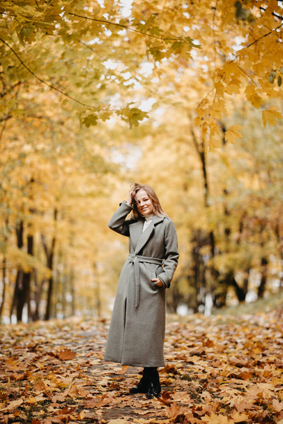Young woman in a gray coat walking in autumn forest  - Photo, image