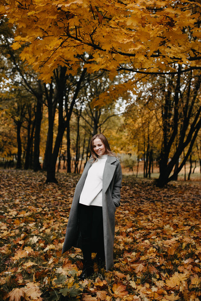 Mladá žena v šedém kabátě kráčející v podzimním lese  - Fotografie, Obrázek