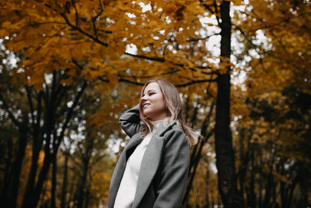 Fiatal nő szürke kabátban sétál az őszi erdőben  - Fotó, kép
