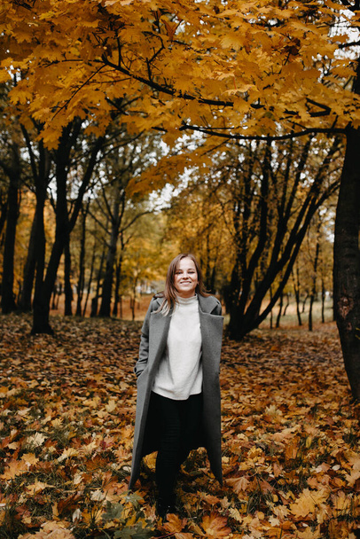 Young woman in a gray coat walking in autumn forest  - Photo, Image