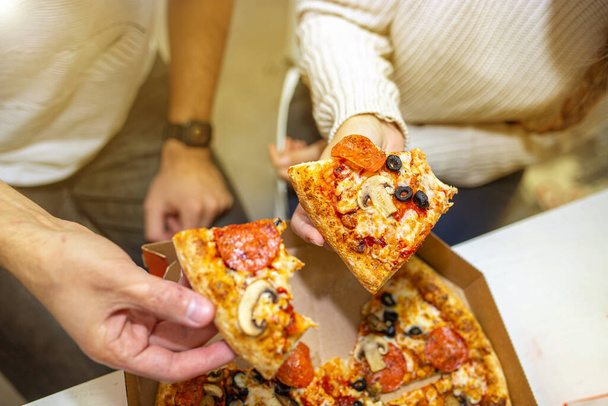 Eating vegetarian pizza with eggplants and olives by a group of people. - Photo, image