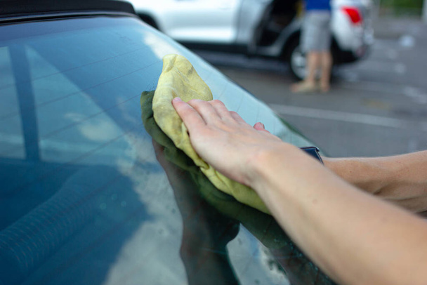 Closeup of male hands cleaning blue car at manual car wash - 写真・画像