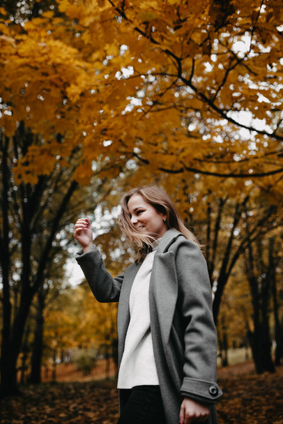 Young woman in a gray coat walking in autumn forest  - Valokuva, kuva