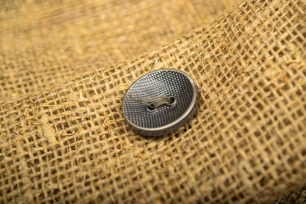 Un botón negro cosido a un pedazo de arpillera. De cerca.
 - Foto, Imagen