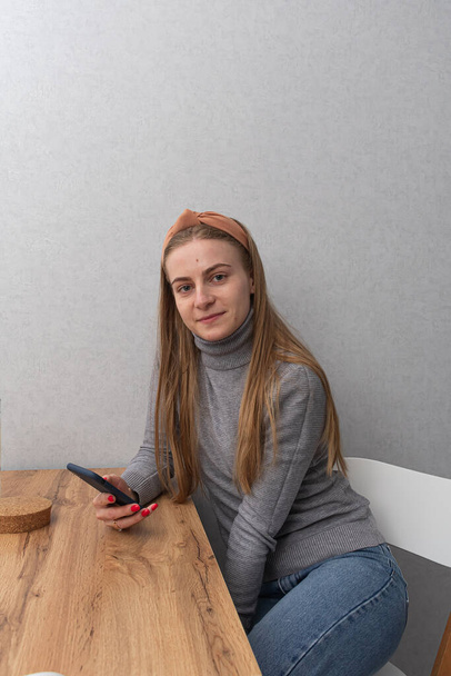 mujer joven sentada en la mesa de madera y usando un teléfono inteligente  - Foto, imagen