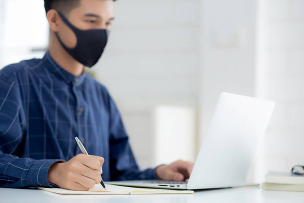 顔のマスクで若いアジアのビジネスマンは、 covid-19を保護し、ノートパソコン上で動作し、ノートブックを書く、家からビジネスマン隔離作業、新しい通常、社会的距離と家にとどまる. - 写真・画像