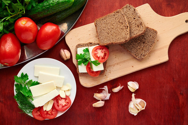 zdrowa żywność - świeży chleb i ser feta na drewnianym tle, pomidory, zielenina i warzywa - Zdjęcie, obraz