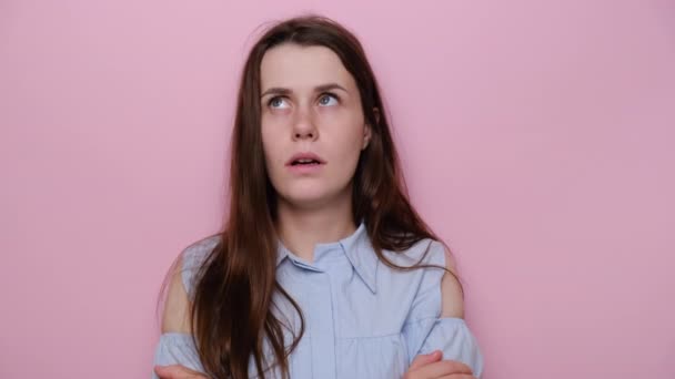 Upset unhappy young woman keeps hands crossed over chest, sad looking at camera and doing sigh. Dissatisfied depressed girl feels offended, wears blue shirt, isolated on pink studio background - Кадры, видео
