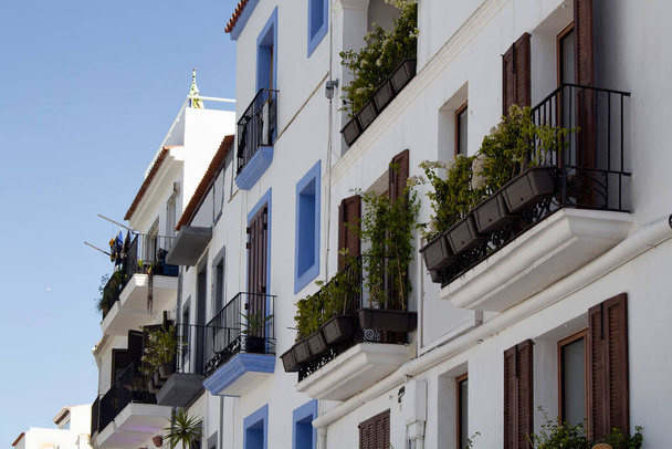 View of traditional, white, typical buildings in Ibiza. The image reflects architectural style of island. Iron made railings and many plants on balconies are in scene. - Fotó, kép