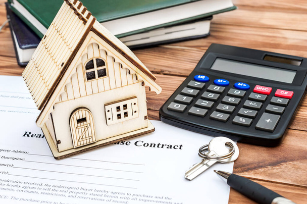 Model of house on business contract with key, calculator, notepads and pen on the wooden table. - Photo, Image