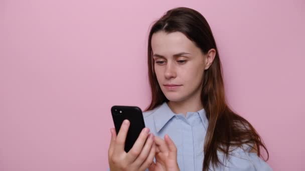 Close up portrait of excited young pretty girl received sms win notification on cellphone. Euphoric millennial woman reading message with good news, celebrating success, isolated on pink studio wall - Video, Çekim