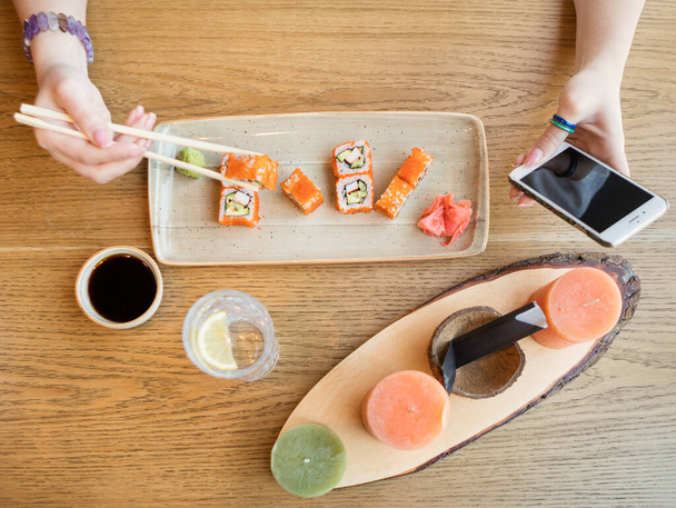 Γυναίκα τρώει σούσι και χρησιμοποιεί smartphone, top view - Φωτογραφία, εικόνα