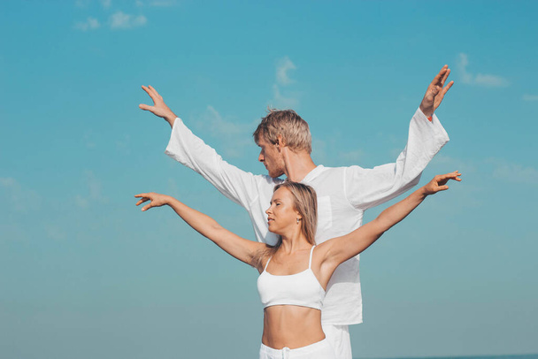 Mies ja tyttö valkoisissa vaatteissa seisovat meren päällä. kädet taitettu namaste - Valokuva, kuva