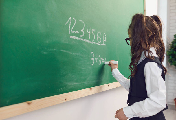 Back to school. A schoolgirl with glasses writes on a school board in a classroom at a lecture. - 写真・画像