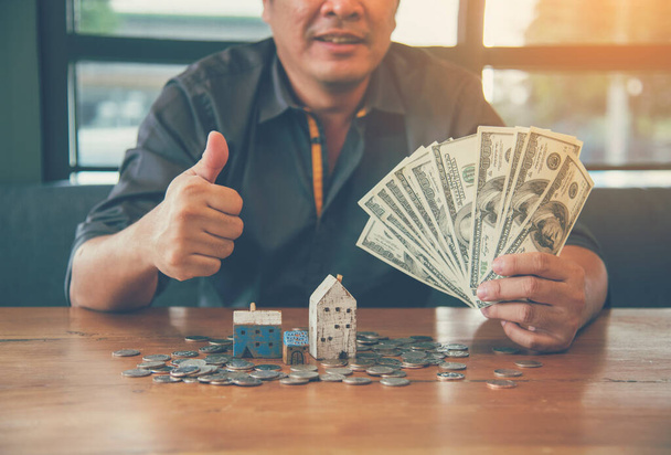 Investment Saving Money Concept. Businessman hold dollar bank note hand on budget to buy house real estate agent. Gold coins stack symbol buy property mortgage money loan with stack of money coin - Photo, Image