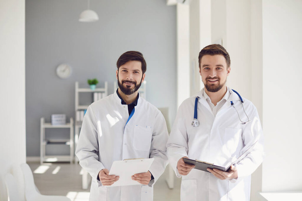 Two practicing doctors with clipboard standing in a clinic office. - Photo, image