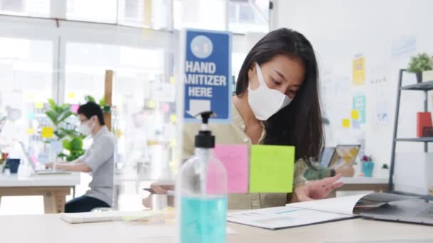 Asiens Unternehmerin mit medizinischer Gesichtsmaske zur sozialen Distanzierung in einer neuen normalen Situation zur Virenprävention, während sie im Büro ihren Laptop wieder bei der Arbeit benutzt. Leben und Arbeit nach dem Coronavirus. - Filmmaterial, Video