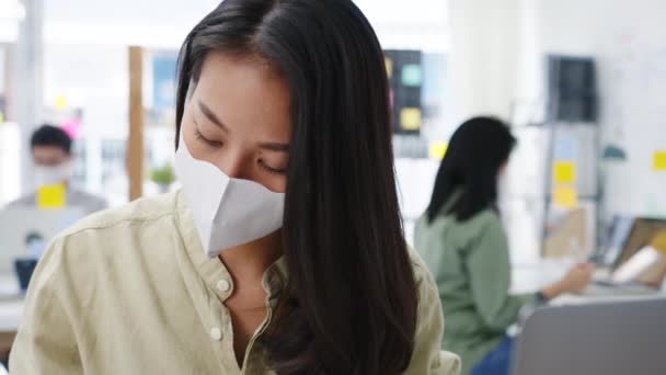 Ázsiai üzletasszony vállalkozó visel orvosi arc maszkot a társadalmi távolságot az új normális helyzetben a vírusmegelőzés, míg a laptop vissza az irodában. Élet és munka a koronavírus után. - Felvétel, videó