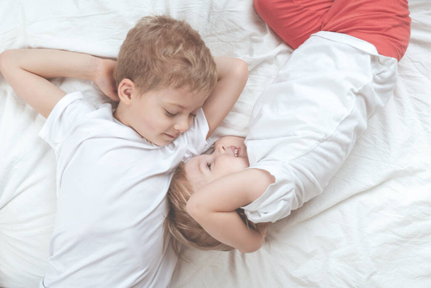 children in white t-shirts lie on the bed. brother and sister together - 写真・画像