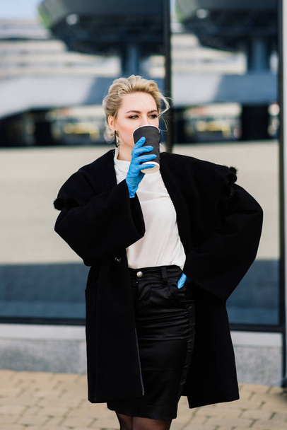 Portret van een jonge zakenvrouw met telefoon, notebook, tablet, koffie buiten. Mooi blond meisje in rubber blauwe handschoenen. - Foto, afbeelding