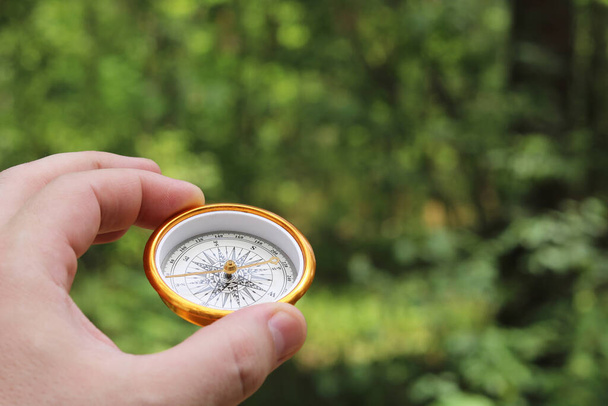 Old classic navigation compass in hand on natural background as symbol of tourism with compass, travel with compass and outdoor activities with compass - Photo, Image