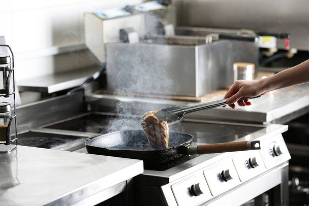 Female chef cooking chicken fillet on stove in restaurant  kitchen, closeup - Photo, image