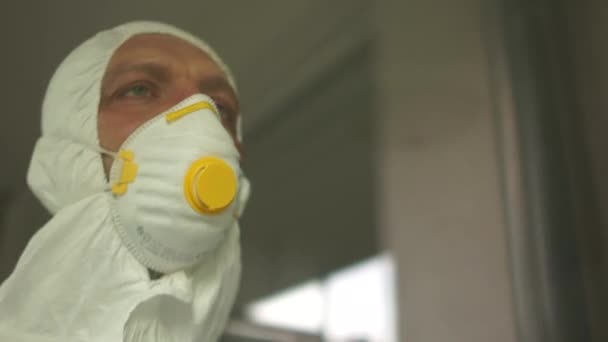 Doctor during a coronavirus pandemic covid-19 takes off glasses and a protective mask, face marks are visible from the mask, red spots. Close portrait of a tired doctor behind the glass - Záběry, video
