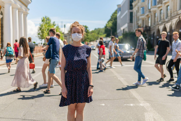 Una chica guapa joven con máscara está de pie cerca de una multitud en una calle cruzando la calle, un montón de gente caminando sin máscaras y no mantener la distancia social
 - Foto, Imagen