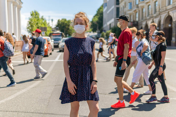 Una chica guapa joven con máscara está de pie cerca de una multitud en una calle cruzando la calle, un montón de gente caminando sin máscaras y no mantener la distancia social
 - Foto, imagen