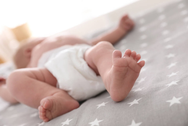 Cute little baby in diaper lying on bed in room, closeup - Φωτογραφία, εικόνα