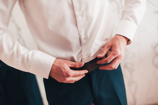Man's hands are worn on pants. Groom, stylish suit business. Wedding. Wear a belt. close up - Photo, image