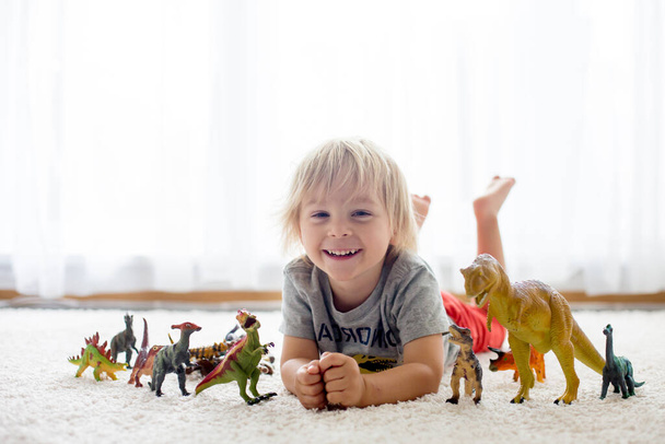 Blond toddler child, playing with dinosaurs at home, nice soft back light - Valokuva, kuva