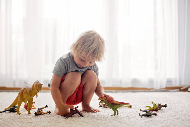 Blond toddler child, playing with dinosaurs at home, nice soft back light - Valokuva, kuva