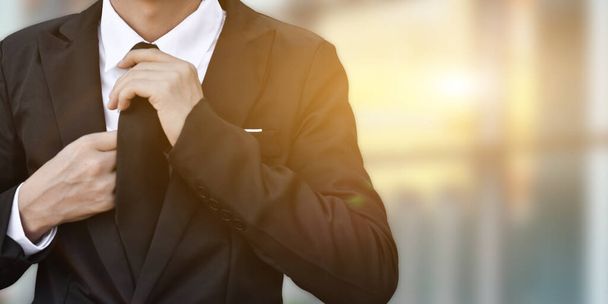 Close-up of businessman in black suit tying the necktie. - Foto, afbeelding